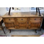 An Old Charm style oak sideboard with three drawers over linenfold carved panelled doors raised on