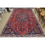 A Persian Mashad small carpet, with large navy floral medallion on a red ground, 290 x 180 cm