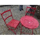 A red painted metal circular terrace table to/w a pair of matching chairs