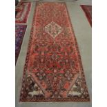 A Persian Hamadan runner, the central wavy lozenge medallion and floral design on red ground