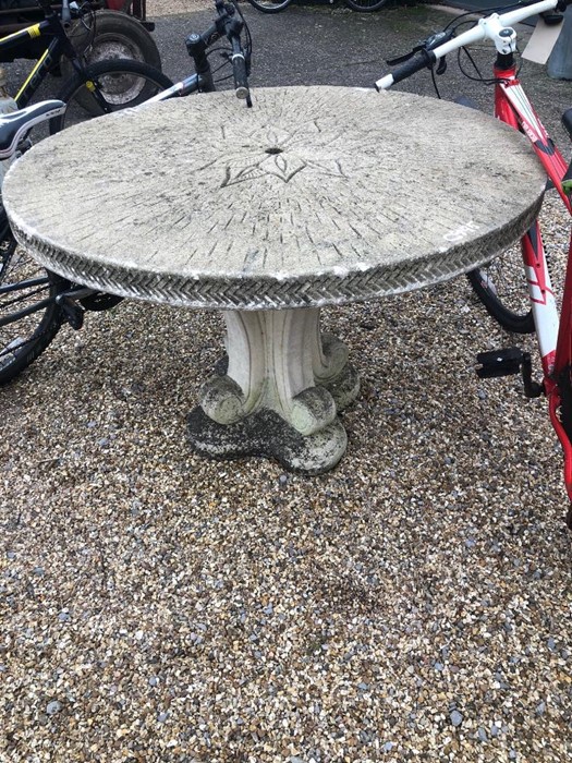 A composite cast stone circular garden table on a shaped quadraform pedestal base