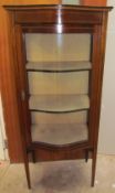 An Edwardian mahogany display cabinet with a shaped top and door on square tapering legs