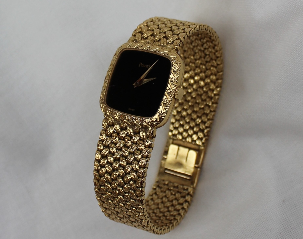 A Lady's 18ct yellow gold Piaget wristwatch, with a black dial and integral bezel and strap,