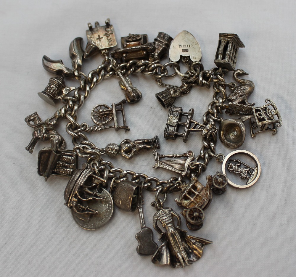 A silver charm bracelet set with numerous charms including a telephone, violin, blackboard, clogs,