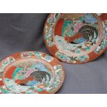A pair of Japanese pottery plates, painted with a cockerel and hen surrounded by flowers,