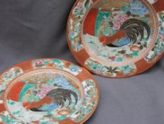 A pair of Japanese pottery plates, painted with a cockerel and hen surrounded by flowers,