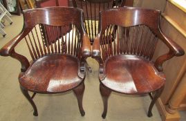 A pair of oak spindle back captains chairs with a scrolling back rail and solid seat on cabriole