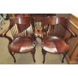 A pair of oak spindle back captains chairs with a scrolling back rail and solid seat on cabriole