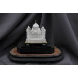 An alabaster model of the Taj Mahal raised on a wooden plinth under a glass dome,