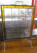 A fire screen with an amber glass and clear glass panel on spreading feet