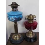 A Victorian oil lamp with a cranberry glass reservoir together with another with a blue glass