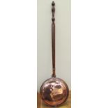 A copper bed warming pan with a turned handle