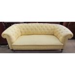 A patterned yellow chesterfield two seater settee on turned legs and casters