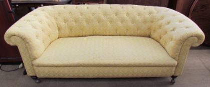 A patterned yellow chesterfield two seater settee on turned legs and casters