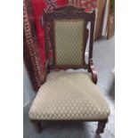 An Edwardian nursing chair with a leaf carved cresting above a pad upholstered back and seat on