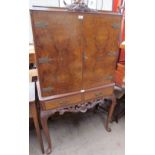 A 20th century walnut cocktail cabinet with a pair of cupboard doors enclosing a mirrored interior