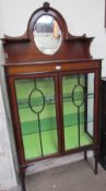 An Edwardian mahogany display cabinet with an oval mirrored back on square tapering legs and spade