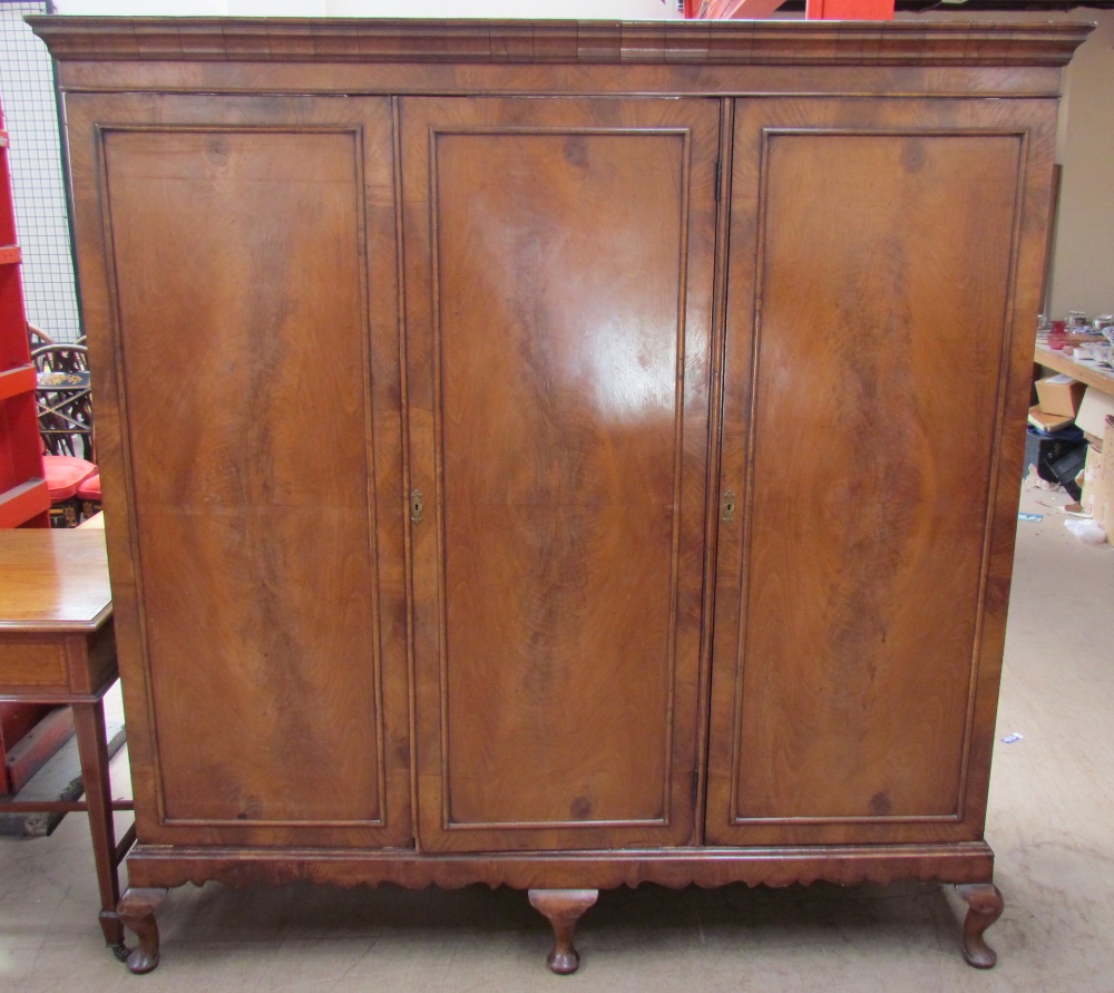 A walnut triple wardrobe with a moulded cornice and three drawers enclosing linen slides,