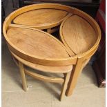 A light teak coffee table of circular form with three oval tables underneath,