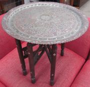 A white metal tray table of circular form with scrolling decoration on a folding base