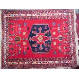 A red ground rug with a central blue medallion and geometric flowers