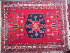 A red ground rug with a central blue medallion and geometric flowers