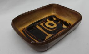 A slipware decorated bowl of rectangular form decorated with a mustard yellow glaze and brown