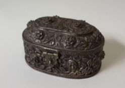 A white metal box and cover of oval form profusely decorated with flower heads and leaves,