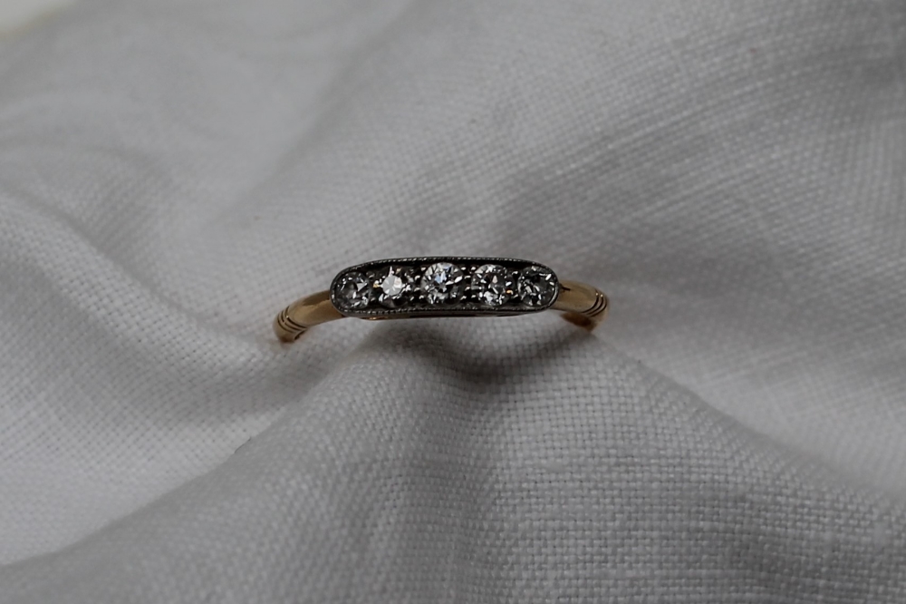 A five stone diamond ring set with five round old cut diamonds to a white metal setting and