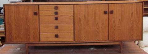 A mid 20th century teak sideboard with three cupboards and five drawers on tapering legs