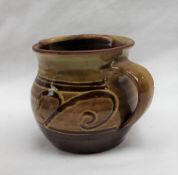 A Sidney Tustin Winchcombe pottery jug, with a mustard yellow glaze, with scrolling decoration,