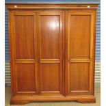 A modern hardwood triple wardrobe with a moulded cornice and three doors on a plinth base