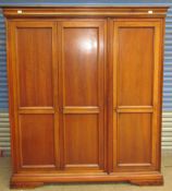 A modern hardwood triple wardrobe with a moulded cornice and three doors on a plinth base