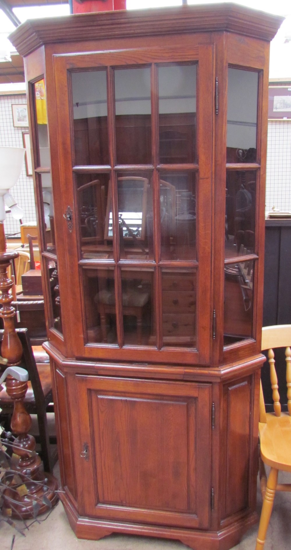 A reproduction oak standing corner cupboard with a moulded cornice above a glazed door,