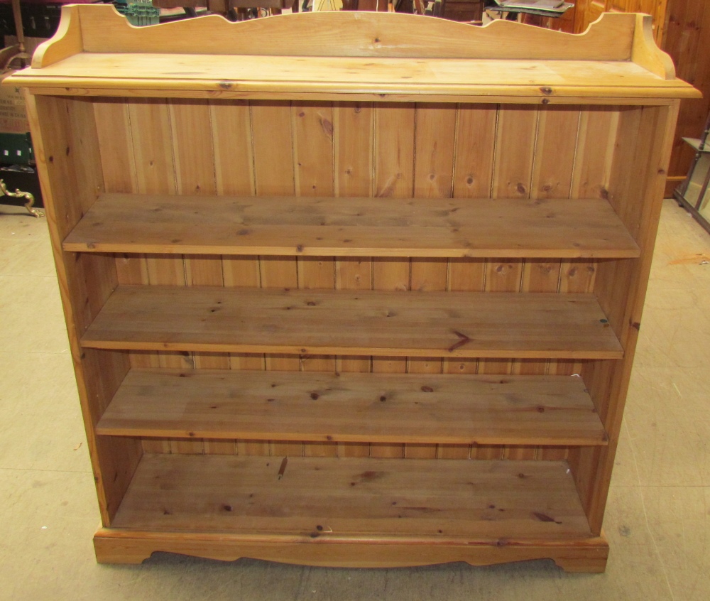 A modern pine bookcase with a shaped top and shaped plinth base