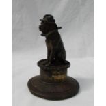 A bronze model of a clown dog wearing a hat and ruff seated on a drum,