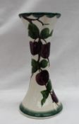 A Llanelly pottery waisted vase with a flared top and spreading base painted with plums on a branch,