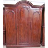 A Victorian mahogany wardrobe with an arched cornice above three panelled doors on a plinth base