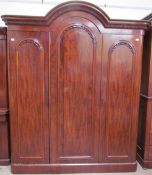 A Victorian mahogany wardrobe with an arched cornice above three panelled doors on a plinth base