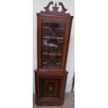 An Edwardian mahogany standing corner cupboard with a broken swan neck pediment above an astragal