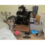 An electroplated three piece tea set together with a candelabra, Polaroid cameras, other cameras,