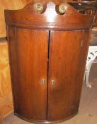 An early George III oak bow front hanging corner cupboard with broken swan neck cresting above a