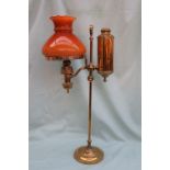A Brass and glass oil lamp, with an orange glass shade and brass column on a spreading foot,