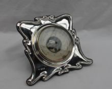 An Art Nouveau inspired silver desk barometer, with a ribbon border, with a central paper dial,