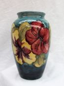 A Moorcroft pottery hibiscus pattern vase with a tapering blue body and pink and yellow flowers,