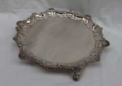 A late Victorian silver salver, with a shell and scrolling border on three claw and ball feet,