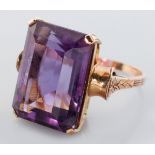 A 9CT YELLOW GOLD AND AMETHYST RING, the emerald cut claw-set amethyst set on floral shoulders and