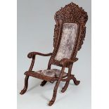 AN INDONESIAN CARVED HARDWOOD FOLDING ARMCHAIR, the high back with pierced latticed carving above an