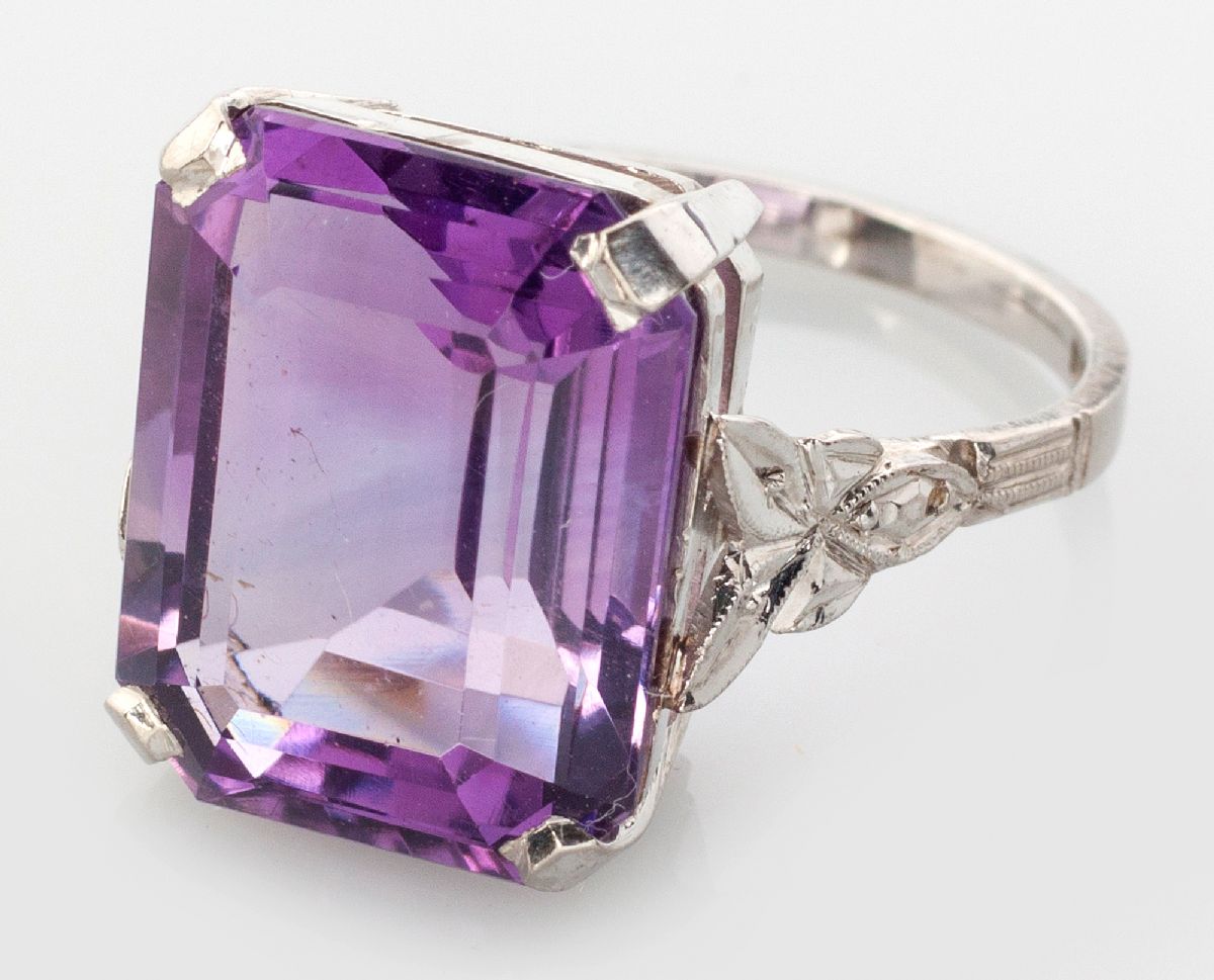 AN 18CT WHITE GOLD AND AMETHYST RING, centre claw-set emerald cut amethyst, the shoulder with leaf