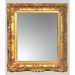 A GILT FRAMED ROCOCO-STYLE MIRROR, the rectangular plate housed within a plain slip and ornately